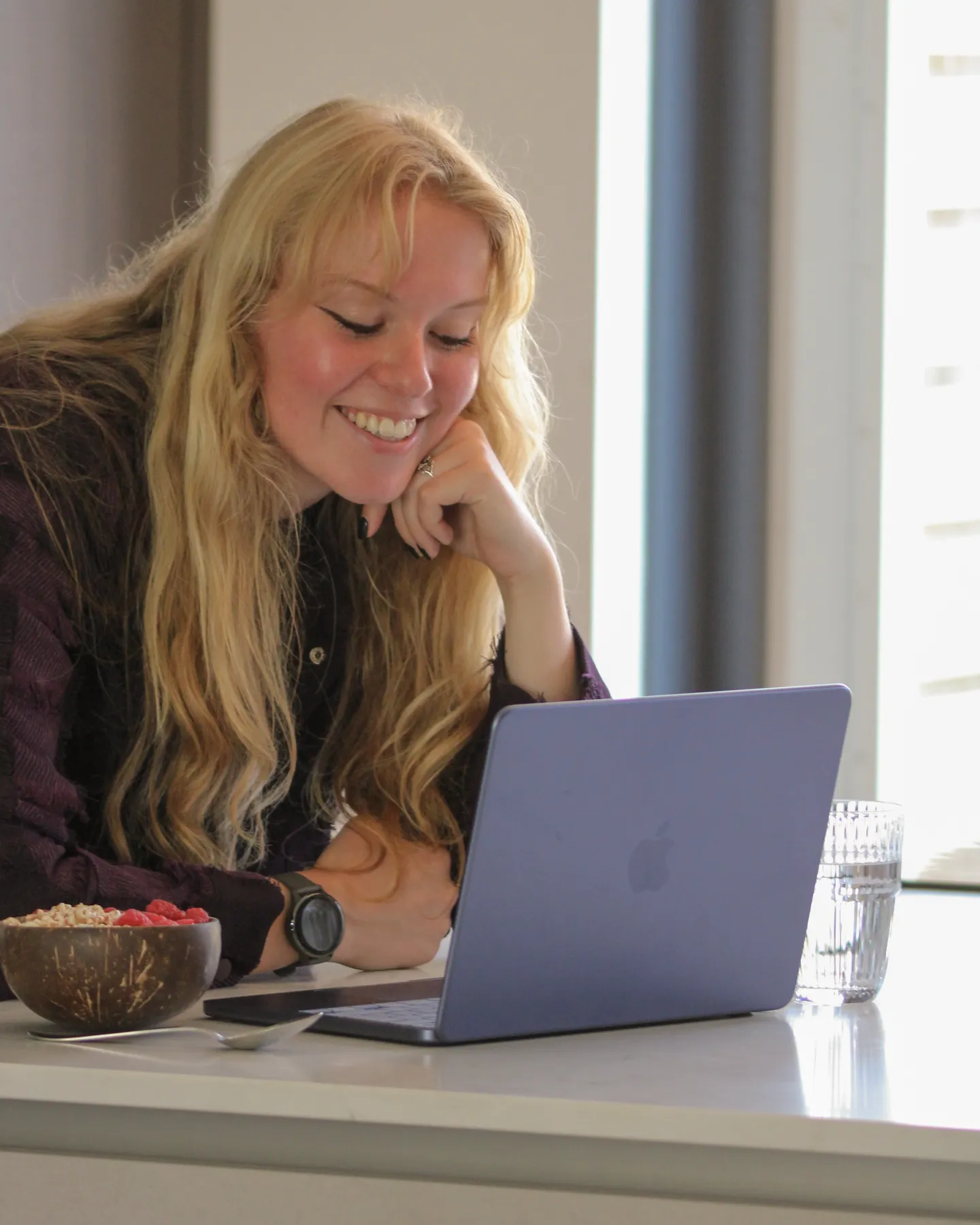 De coach lacht achter haar laptop aan de keukentafel.